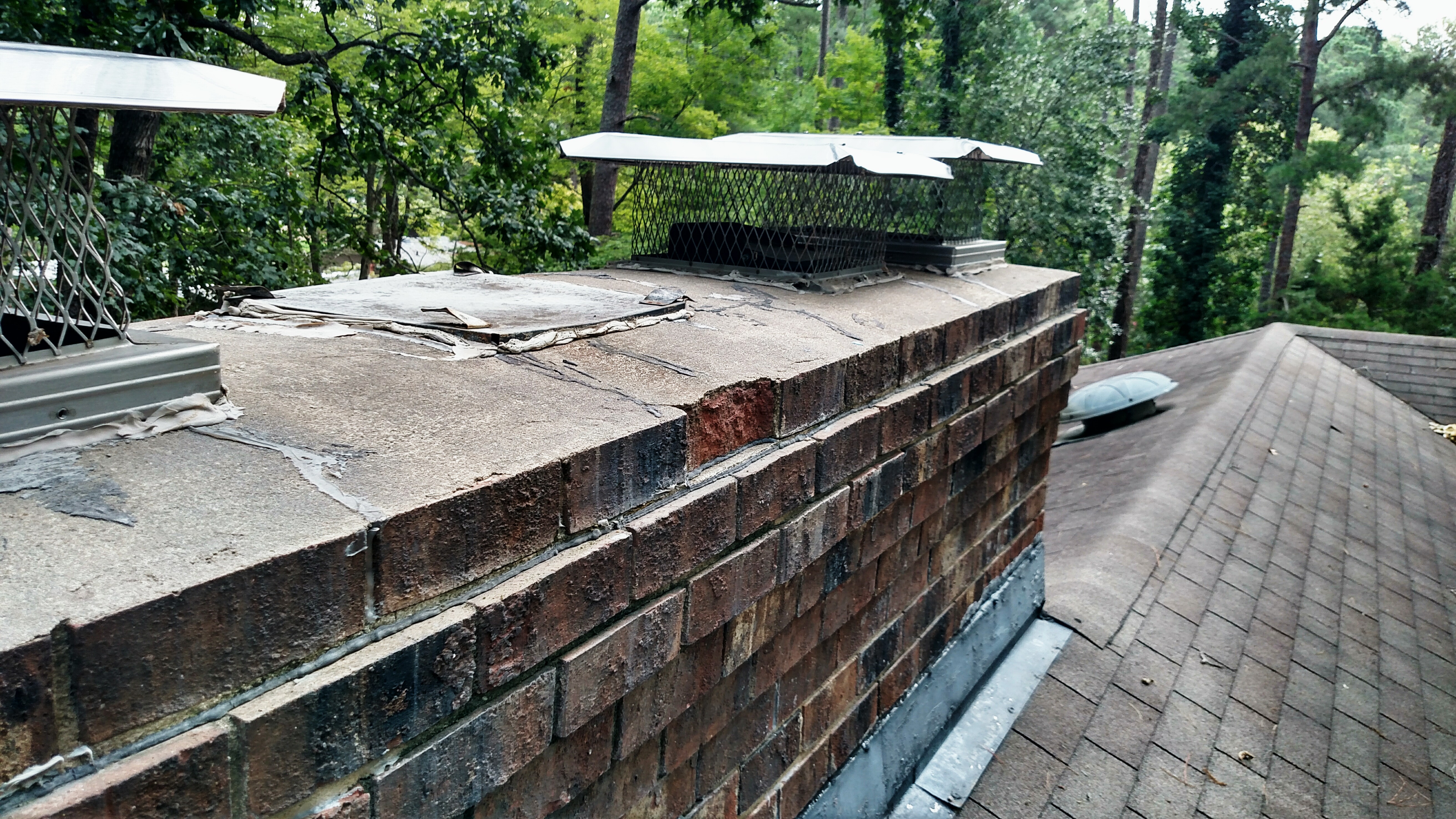 Spalling brick chimney with three crowns can cause leaks woods in background
