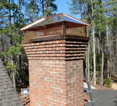 Copper Cap Installation on nice chimney with ladder and woods in background
