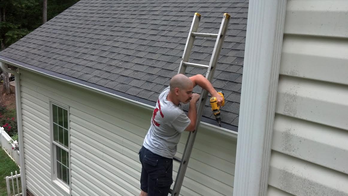 Man installing gutter guards on ladder on white house